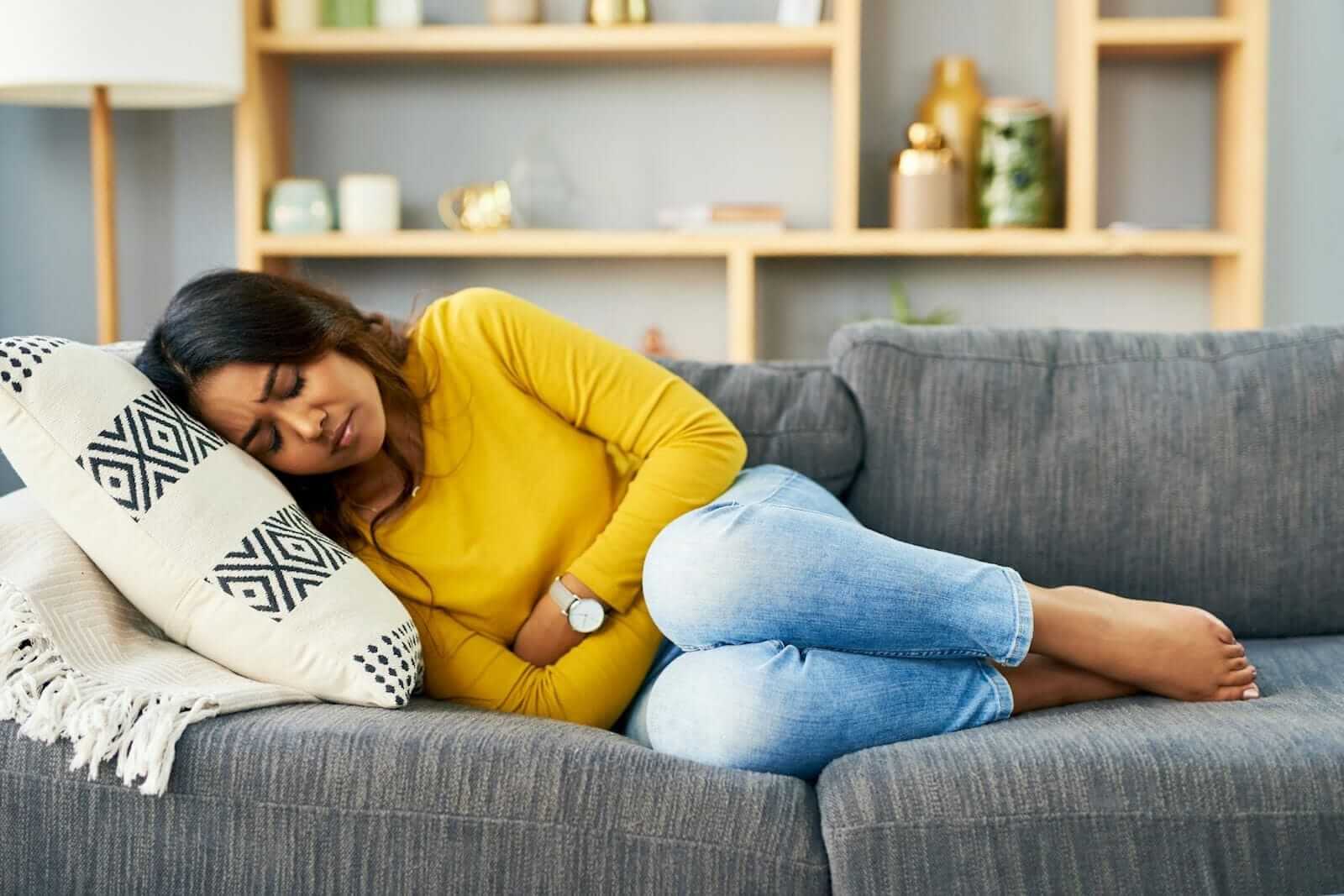 Woman holds arms over her stomach in pain laying on couch
