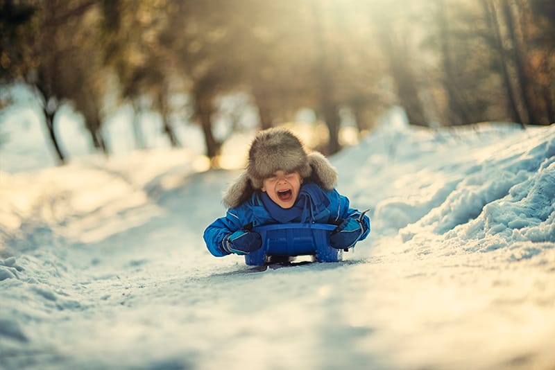 Happy child sledding down the hill on a winter day