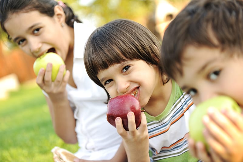 Three children happily eating apples outside