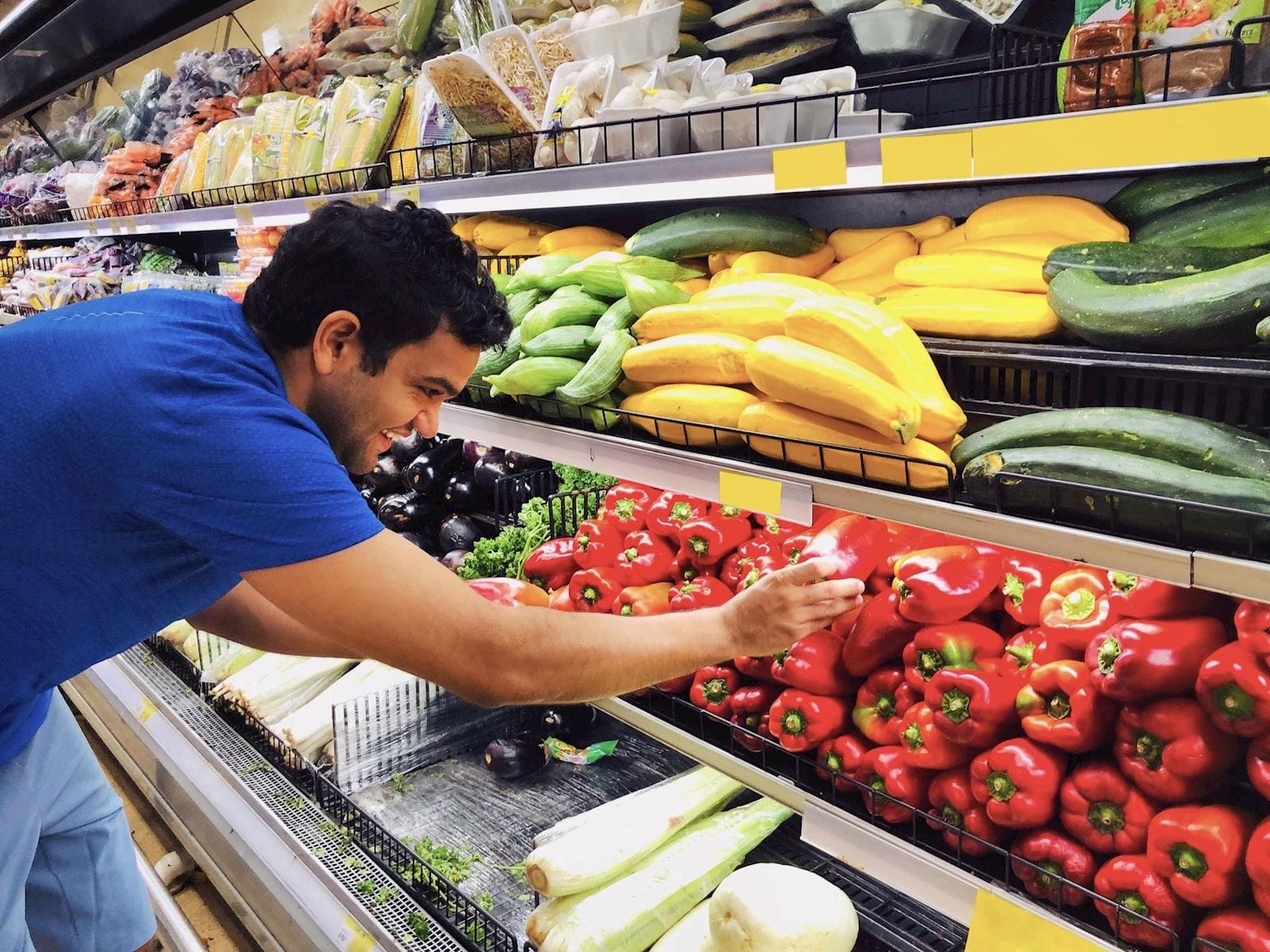 man selects red pepper from produce section at grocery store