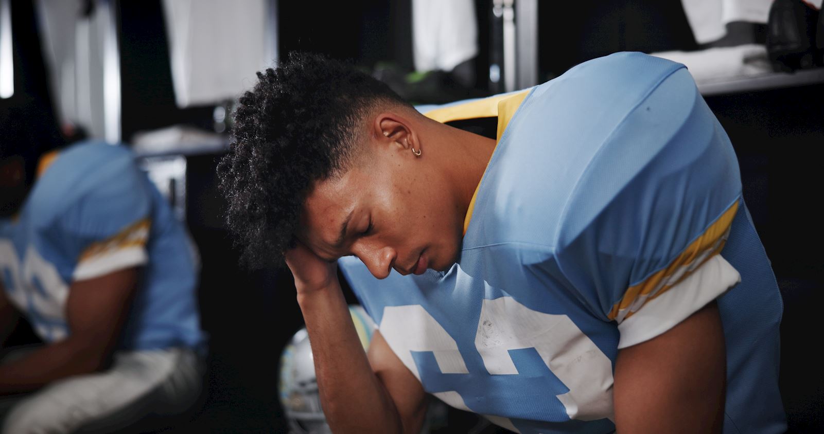 football player sitting down holding his head