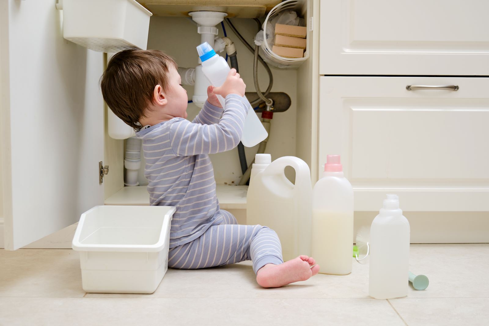 child playing with cleaning products by cabinet