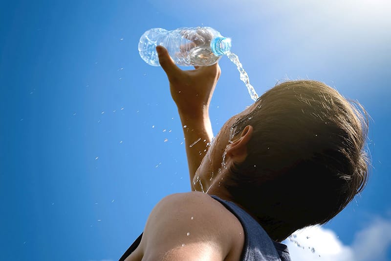 man outside pouring water bottle on face to cool off