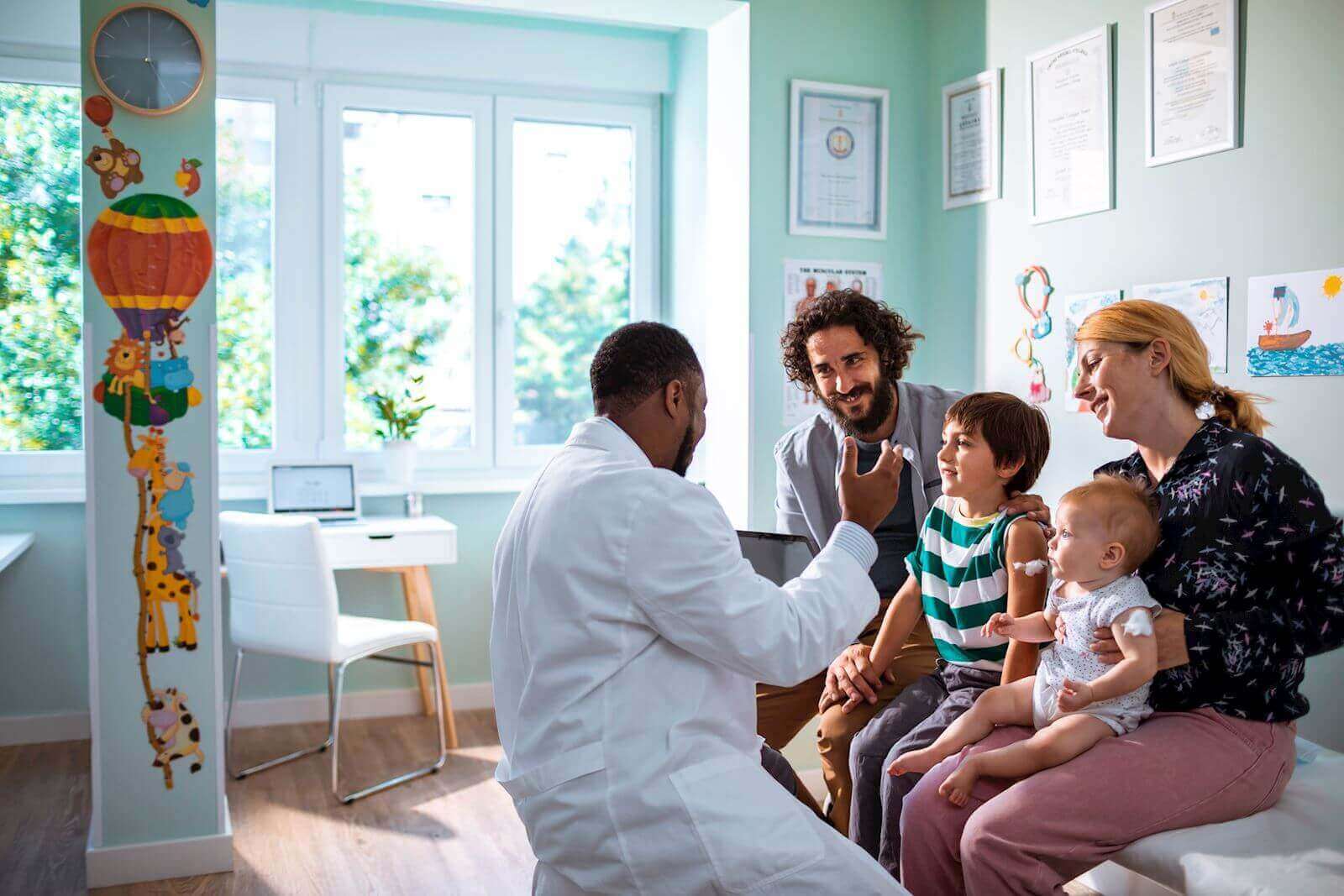 Pediatrician and father, mother, school-aged boy and baby girl sit in pediatrician's office