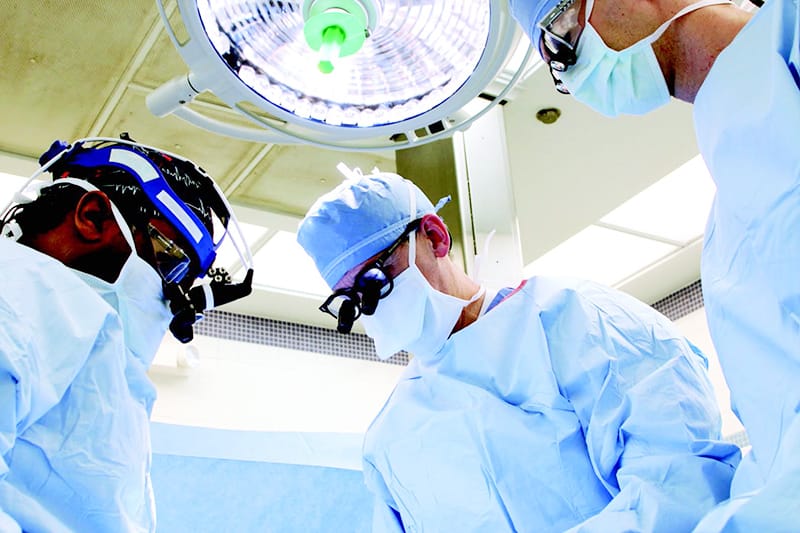 Three physicians with surgical masks on, performing surgery