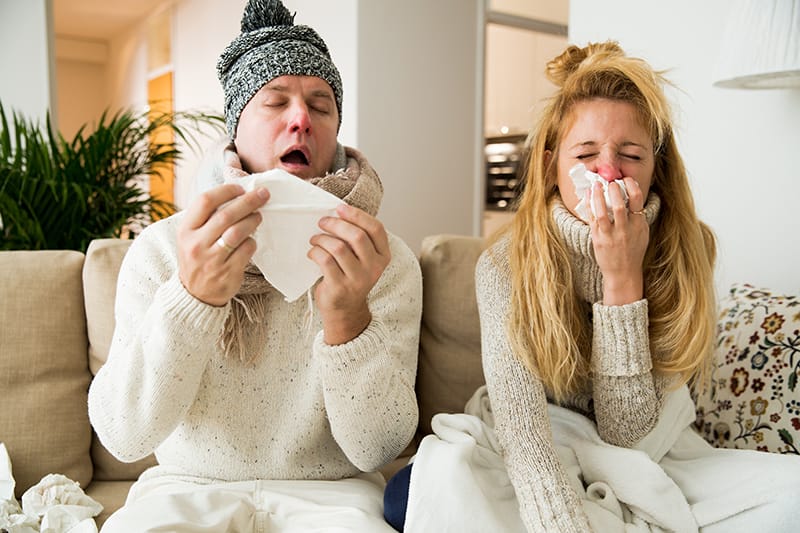 Man and women sick on the couch, coughing and sneezing