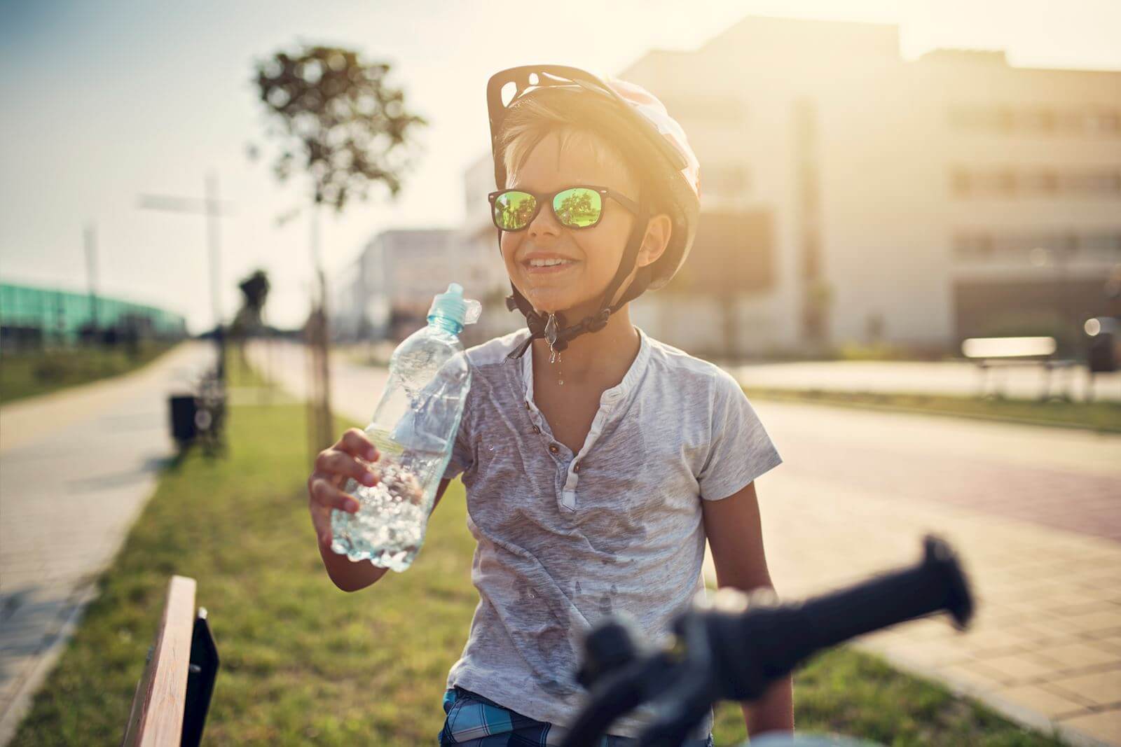 Young boy on a bike drinks water in the sunshine