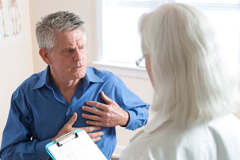 Concerned looking man with hands on chest while meeting with a physician