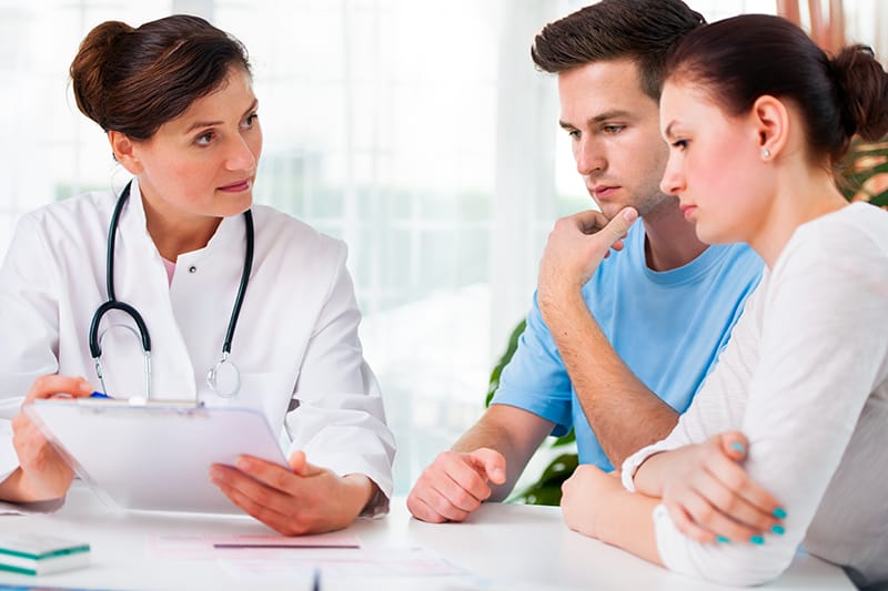 Doctor sitting with couple, showing medical charts