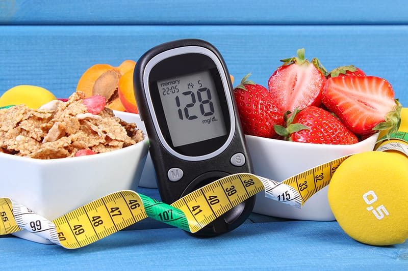Blood glucose meter with fruit, whole grains, a dumbell and a measuring tape