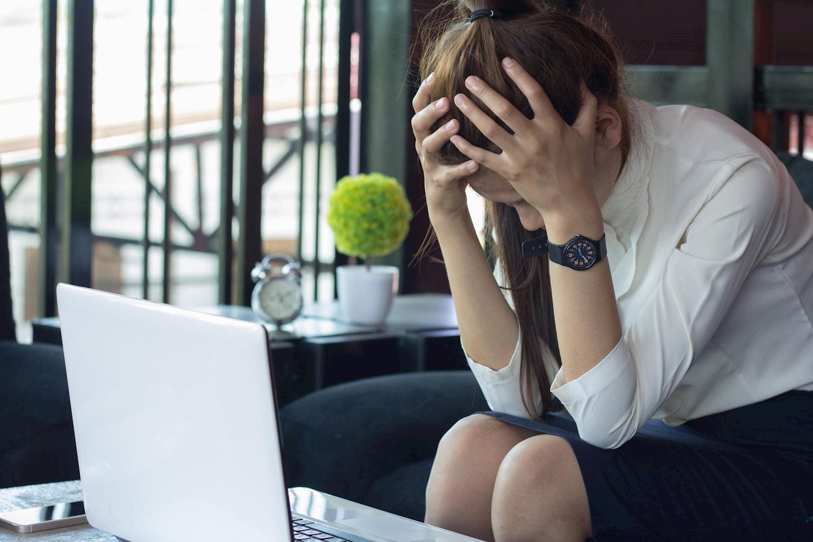Stressed woman sits with her heads in her hands in front of her laptop computer