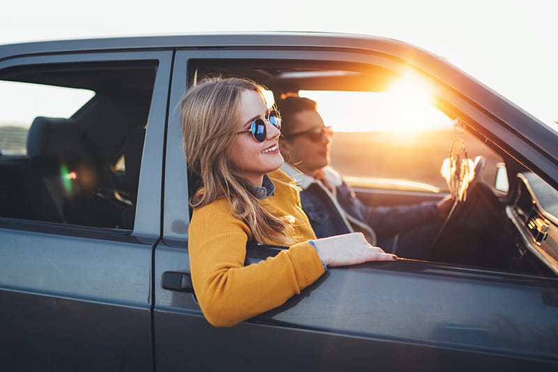 Couple in a car, traveling with their windows down during a sunset