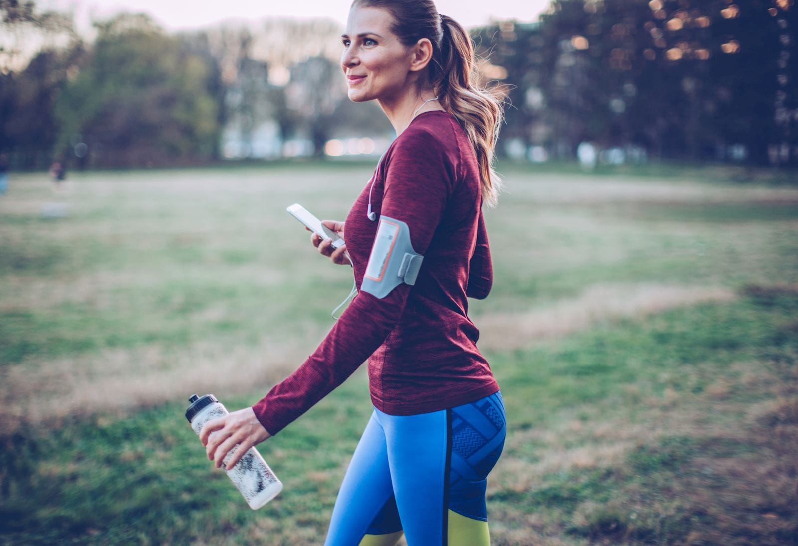 Woman walking in the park while holding a cell phone and water bottle