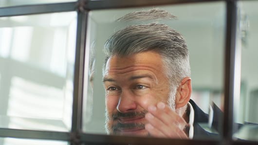 Man pulling on face while looking in the mirror